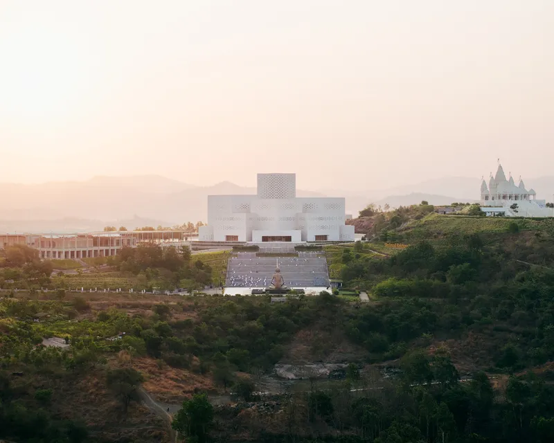 White perforated cube volume on a hillside terrace with mountains in the hazy distance at dusk