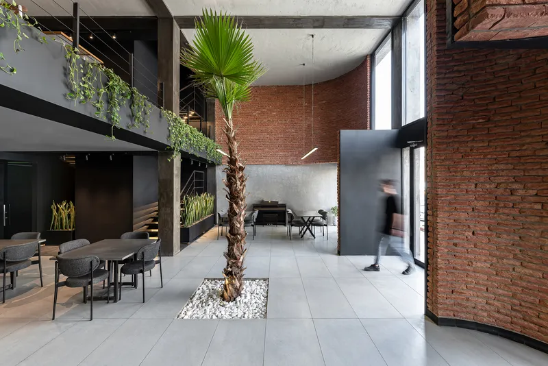 Double-height interior with exposed brick walls, planted palm tree and a person walking past the mezzanine