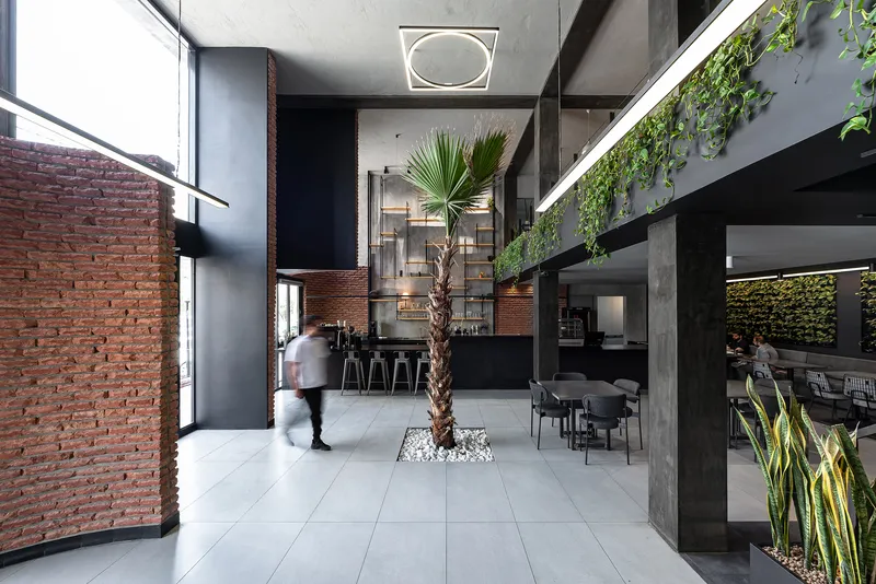 View toward the bar counter through the double-height space with a person in motion near the palm