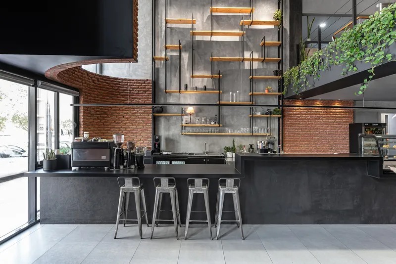 Cafe counter with metal stools facing timber and steel shelving mounted on concrete and brick walls