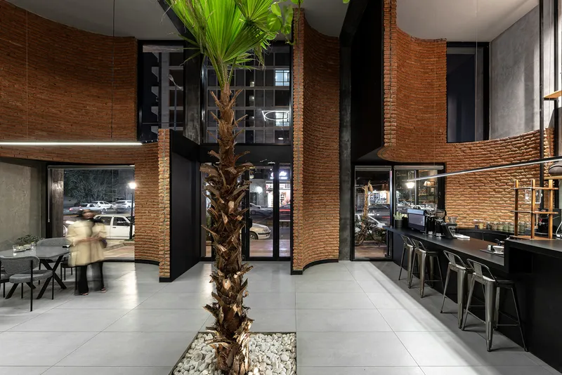 Double-height interior space with curved brick columns, palm tree planter, and bar seating at night