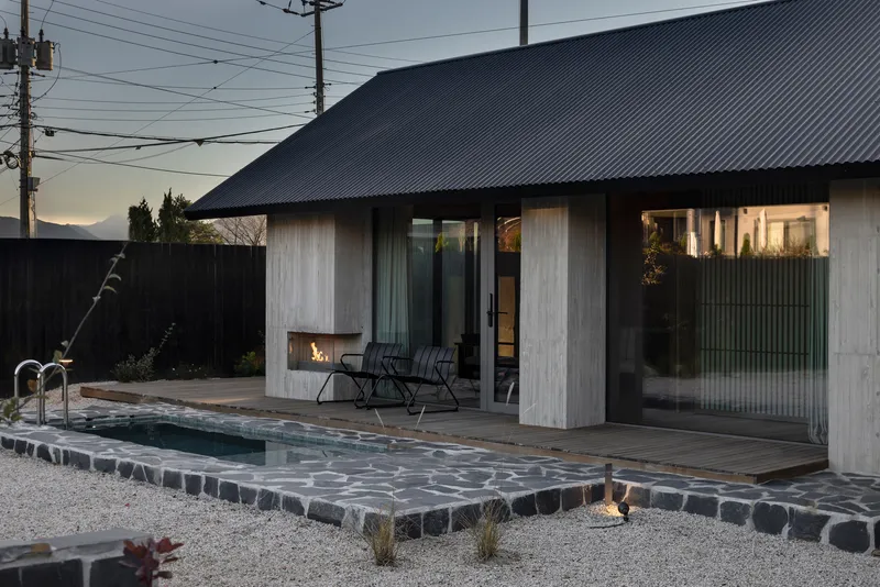 Courtyard with lap pool and basalt stone paving alongside weathered timber pavilion at dusk