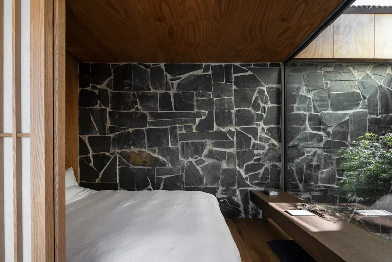 Bedroom with dark basalt stone wall and glazed opening to planted courtyard garden