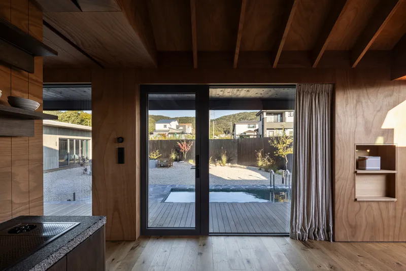 Kitchen with exposed timber rafters looking through glass doors to gravel courtyard beyond