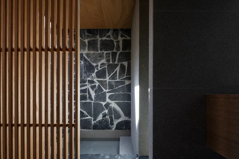 Vertical timber slat partition beside a dark stone wall with dramatic side lighting at dusk