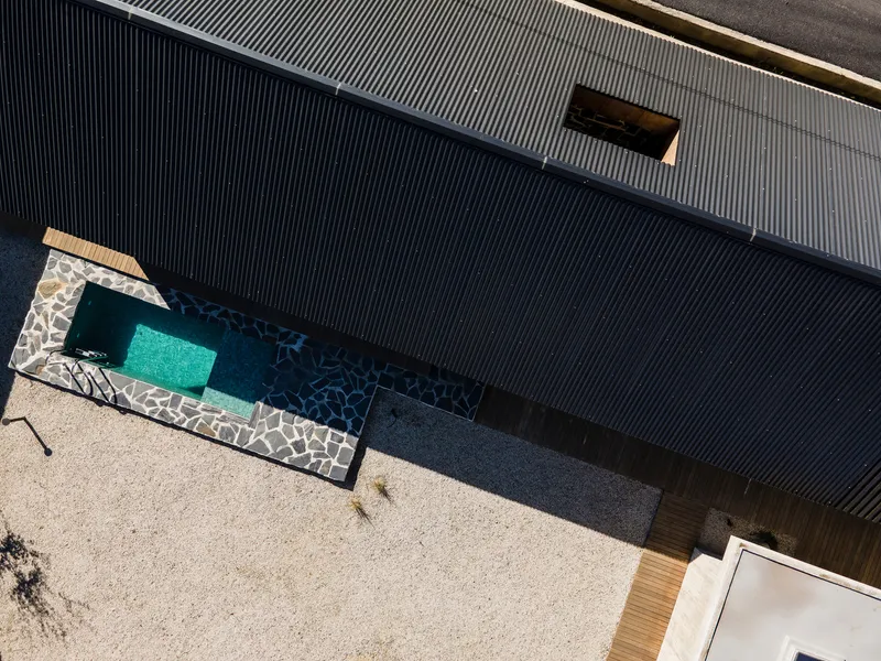 Overhead view of a courtyard pool with stone edging and corrugated metal cladding in bright sunlight