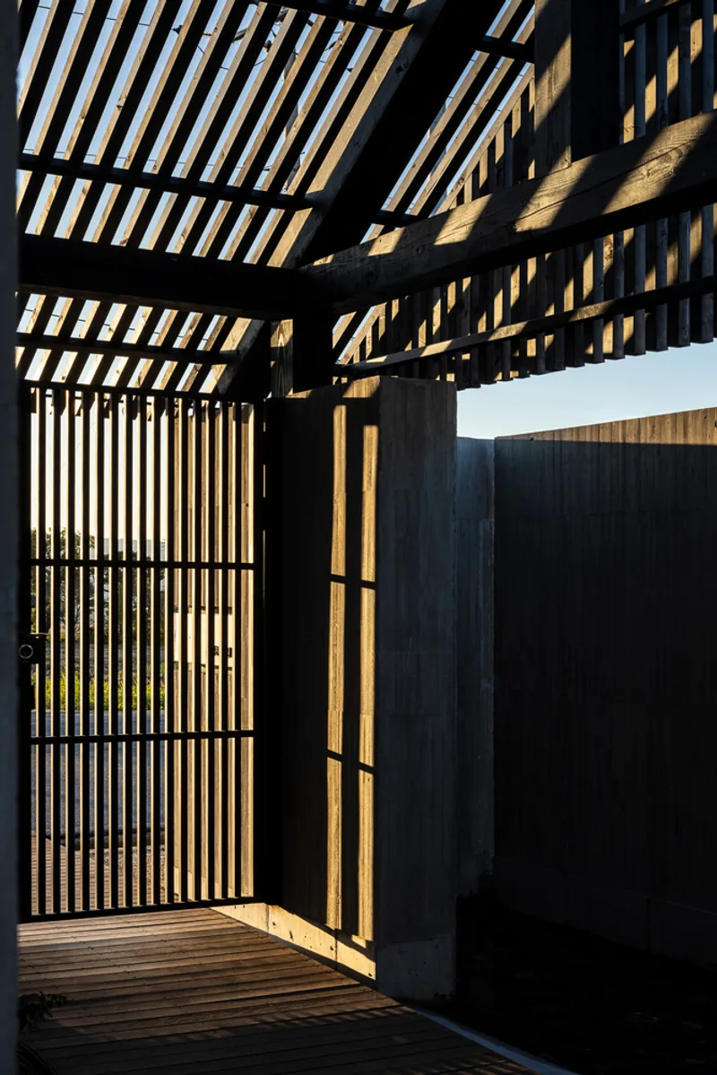 Slatted timber pergola overhead casting shadows on the deck at the entrance threshold