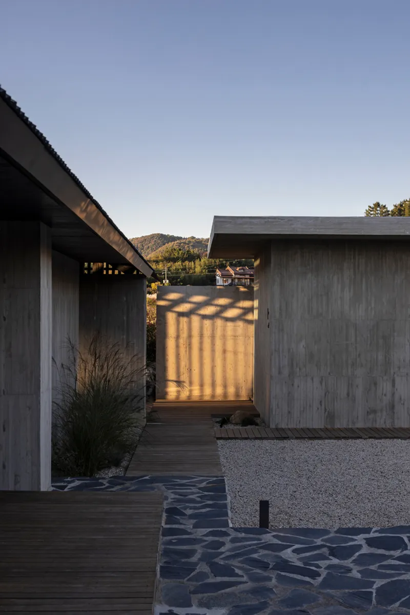 Courtyard passageway between timber-clad volumes with stone paving and low grasses in late afternoon light