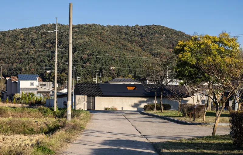 Street approach to the low-pitched roof structure with hillside and bare trees in background