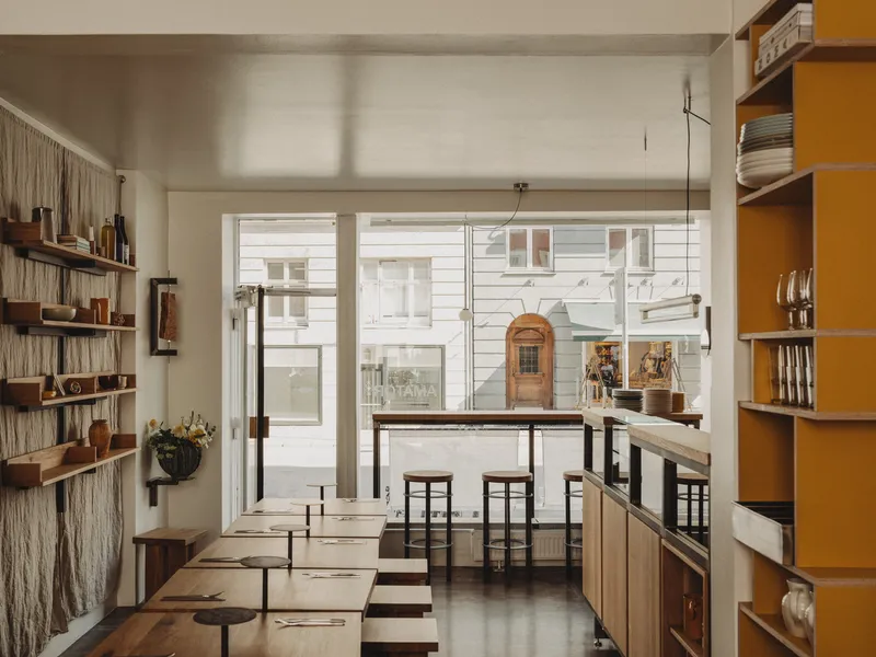 Interior view through dining area with timber shelving and glass doors overlooking a white-painted street facade