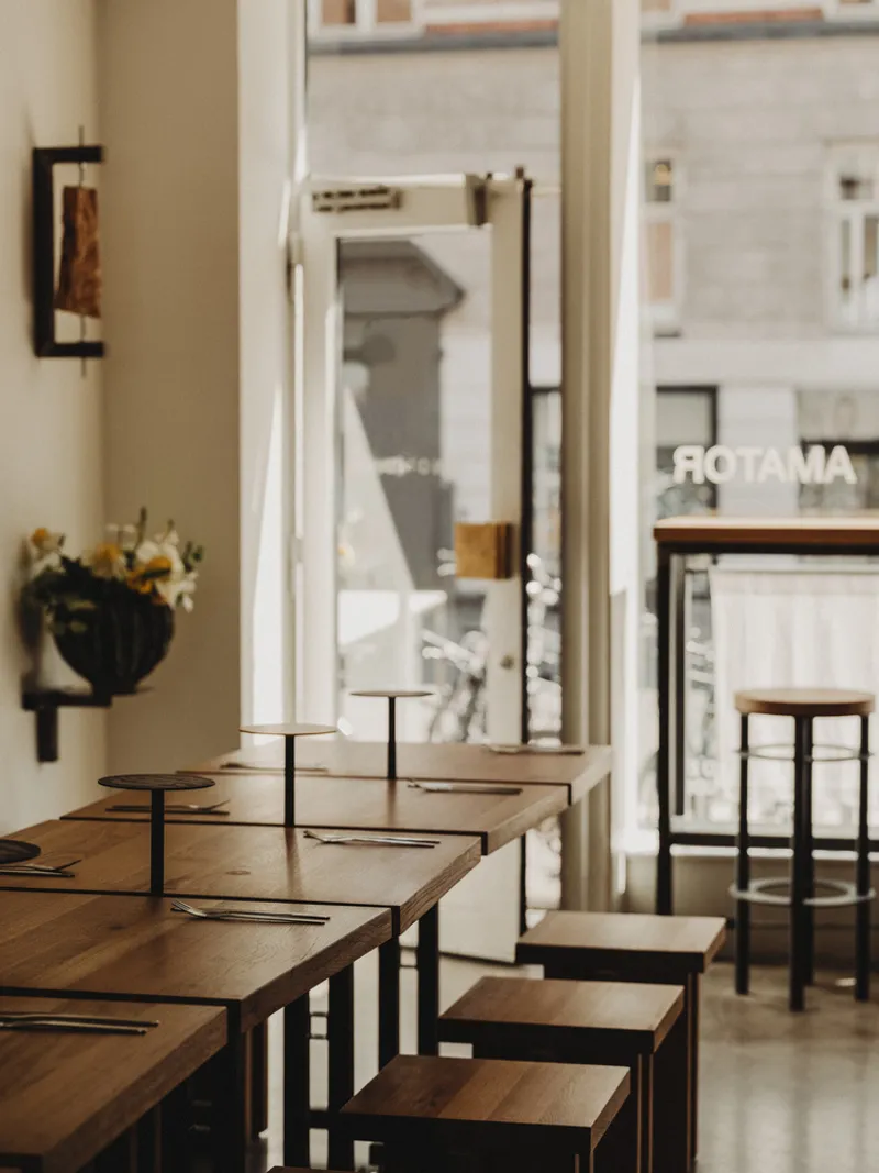 Oak dining counter with steel-framed stools by open glass door with view to street storefront across the way
