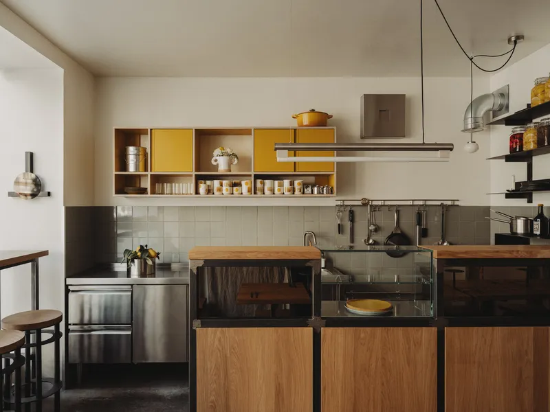 Kitchen wall with yellow accent cabinets, white tile backsplash and stainless steel range hood above oak island