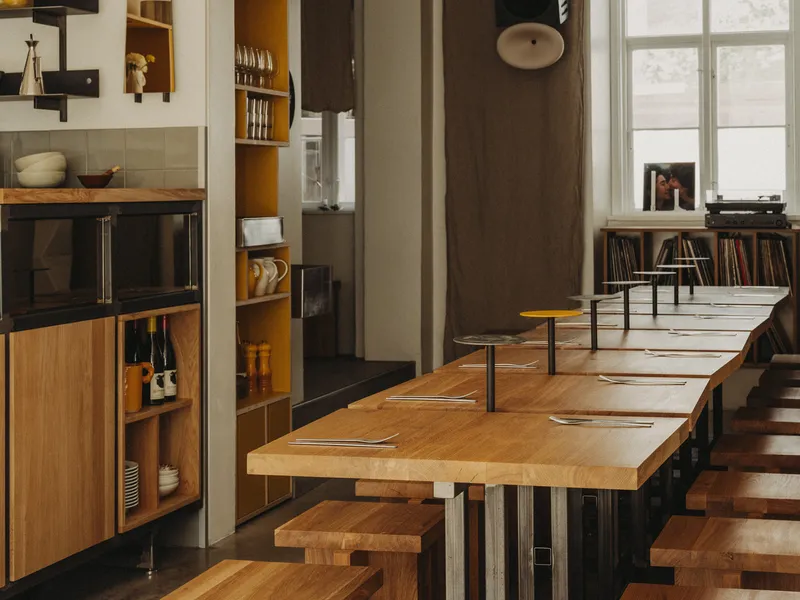 Timber dining counter with steel frame stools looking through doorway to window-lit adjacent room