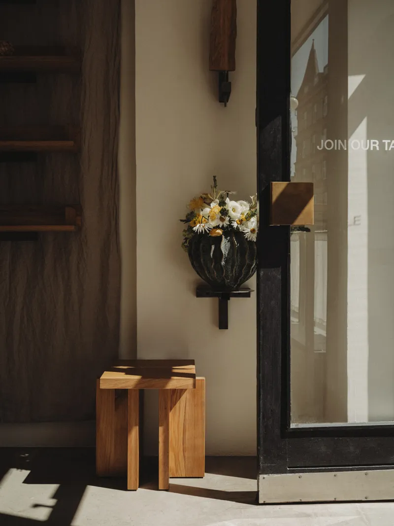 Wall-mounted planter with flowers beside a timber stool in afternoon sunlight