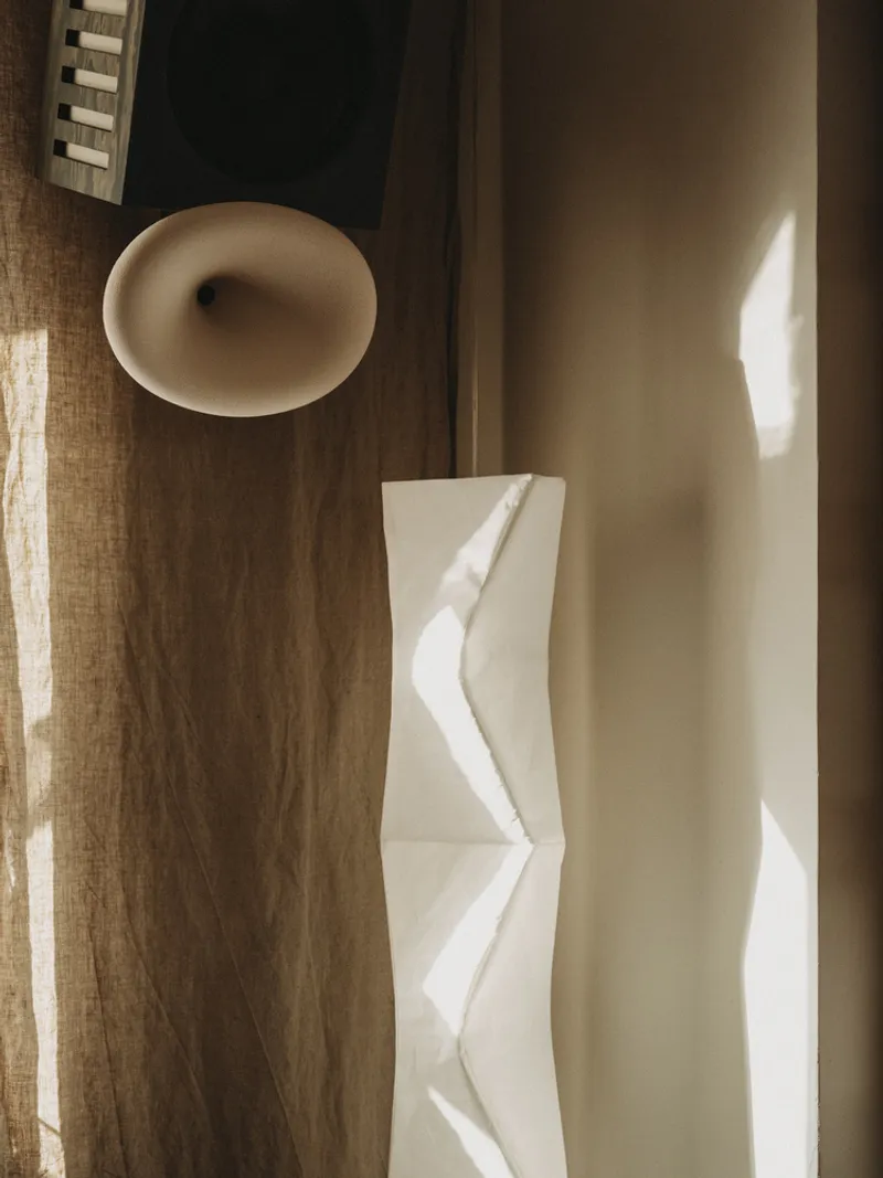 Walnut wood paneling with oval sconce and folded paper sculpture in soft afternoon light