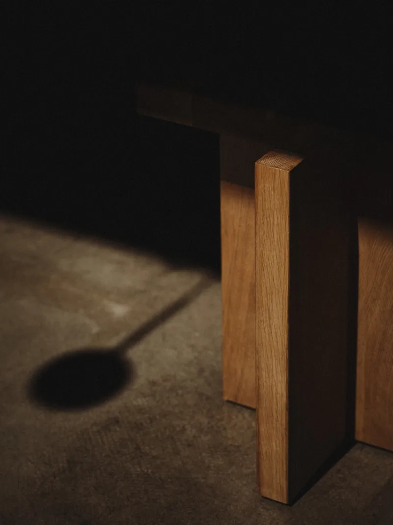 Oak table legs meeting a dark cabinet base with diagonal sunlight across the floor