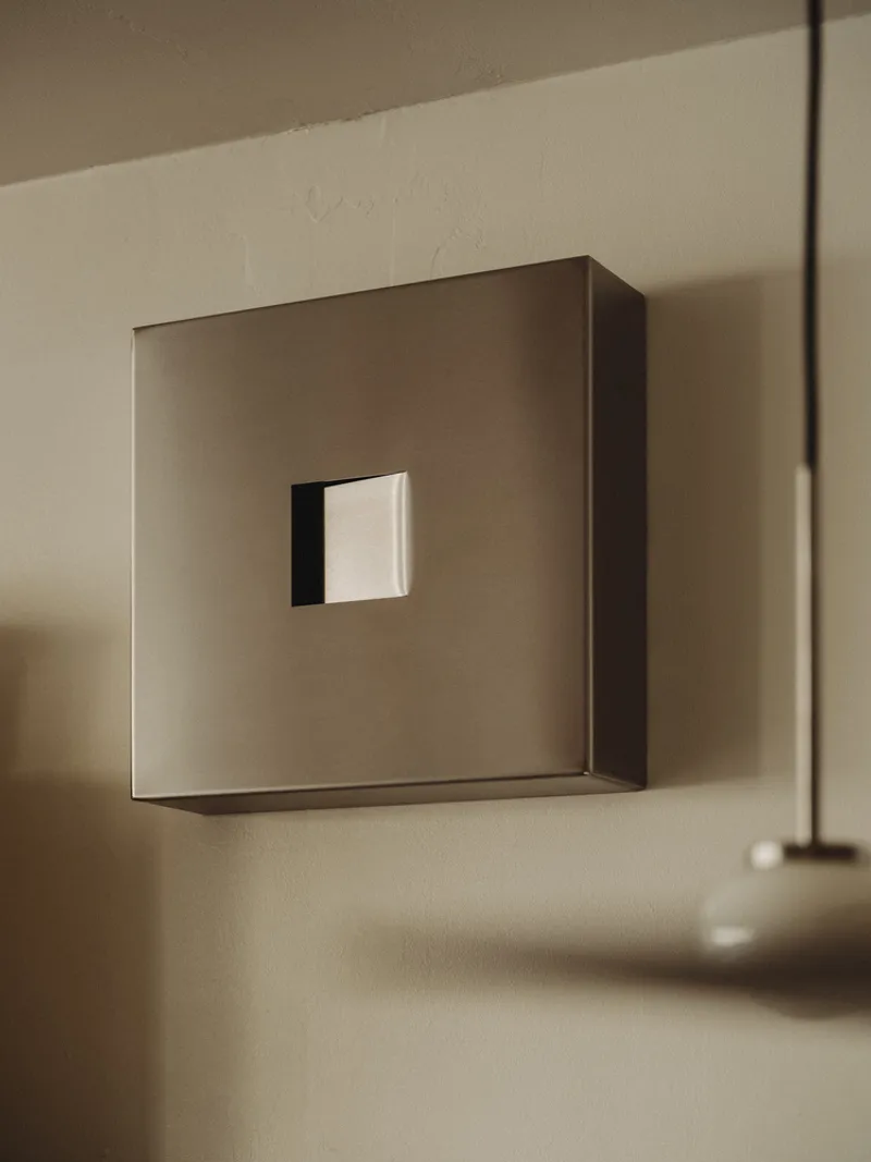 Brushed metal square sconce with recessed opening mounted on a white wall