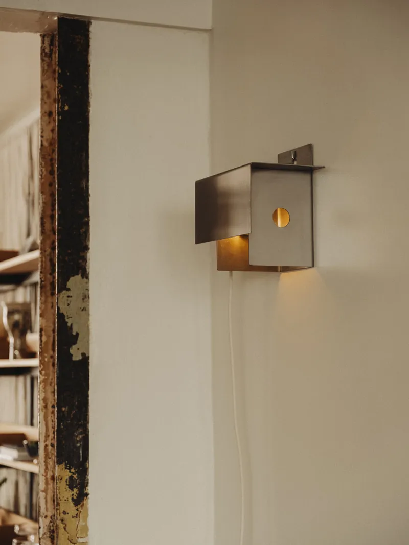 Metal box wall sconce with circular aperture beside an exposed weathered timber beam
