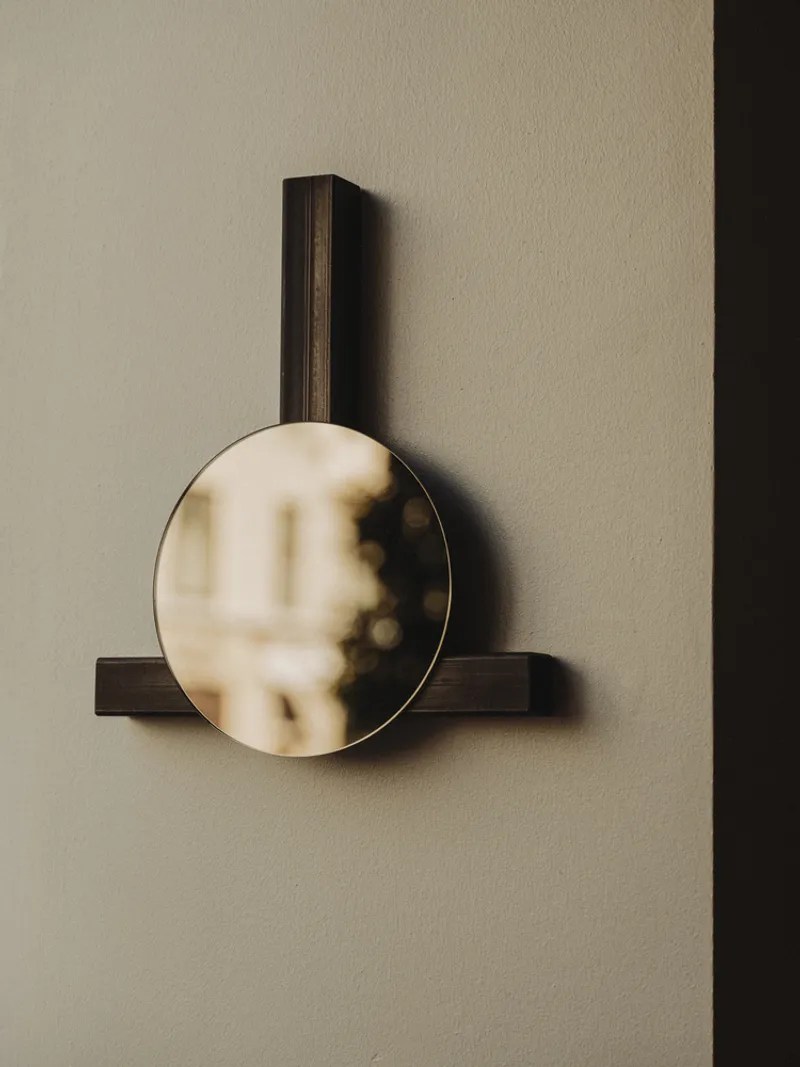 Circular mirror mounted on dark wood brackets against a cream plaster wall