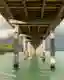 This architectural image showcases a wooden pier extending over calm, turquoise waters. The pier's s