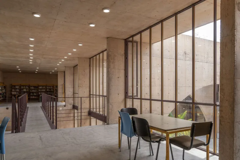 Interior mezzanine reading area with steel-framed glazing overlooking a concrete courtyard and library shelves