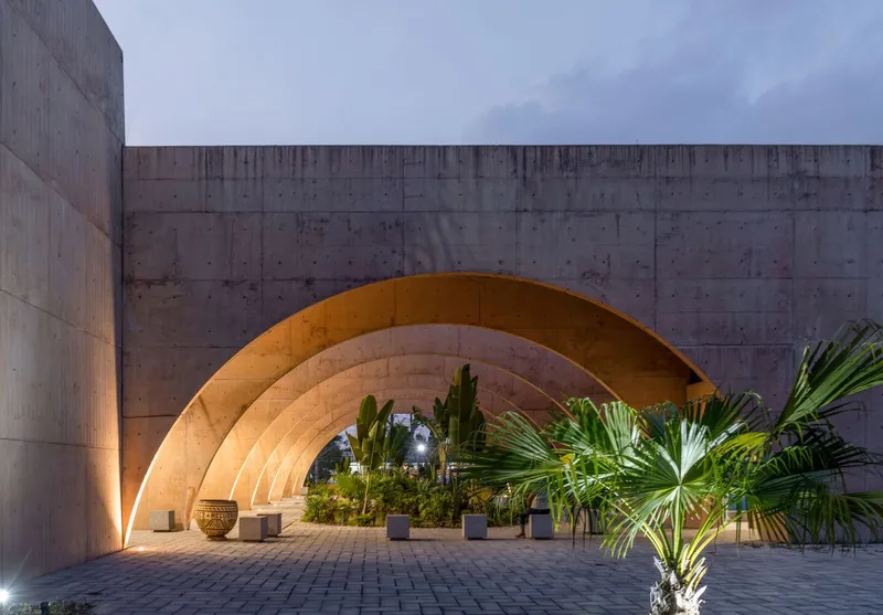 Covered courtyard with laminated timber arches framing palm trees and planters at dusk