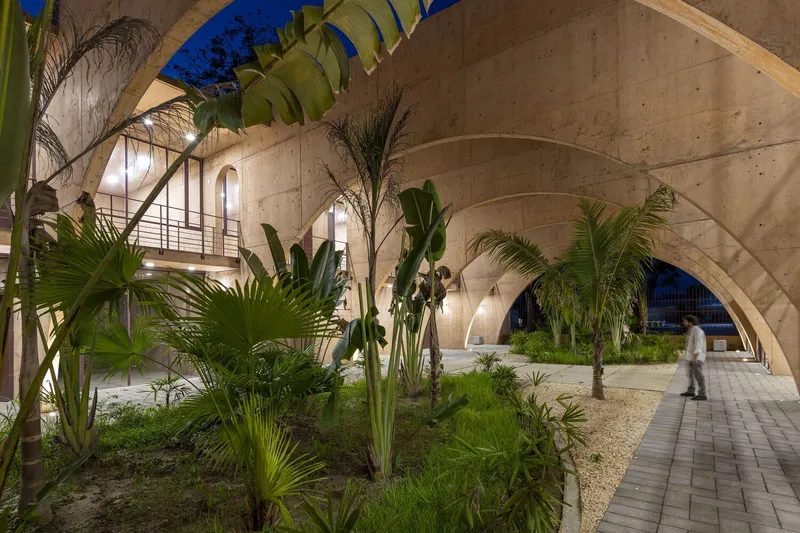 Landscaped courtyard with tropical planting beneath laminated timber arches and concrete walkways at twilight