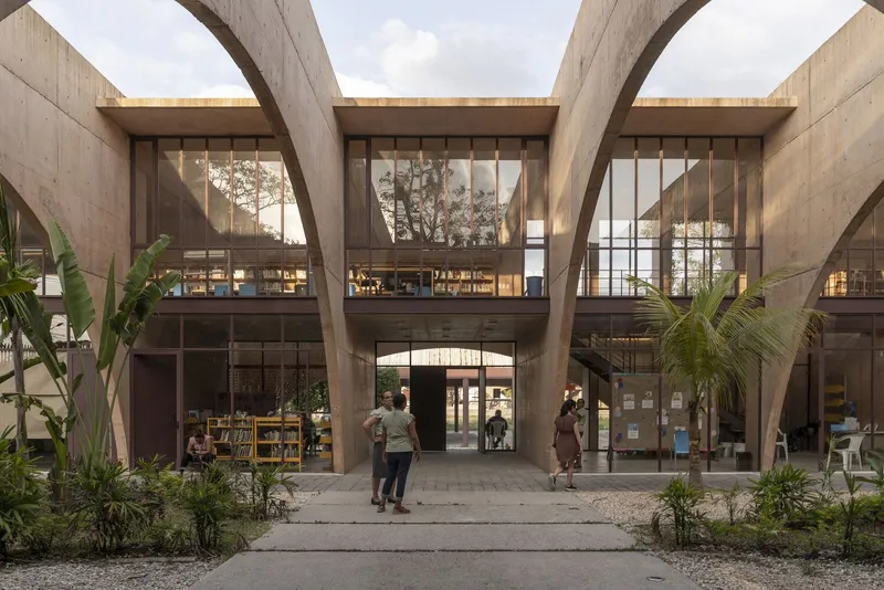 Courtyard entry framed by massive concrete arches with palm trees and visitors on paved pathways