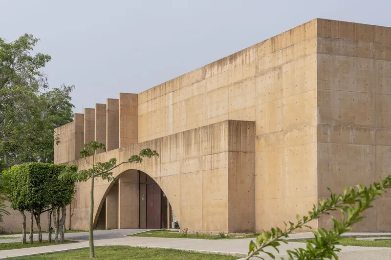 Stepped concrete facade with arched openings flanked by young trees under overcast sky