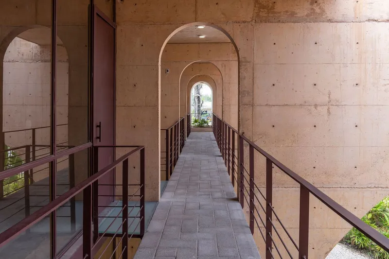 Elevated bridge with metal railings passing through sequence of concrete arches toward garden