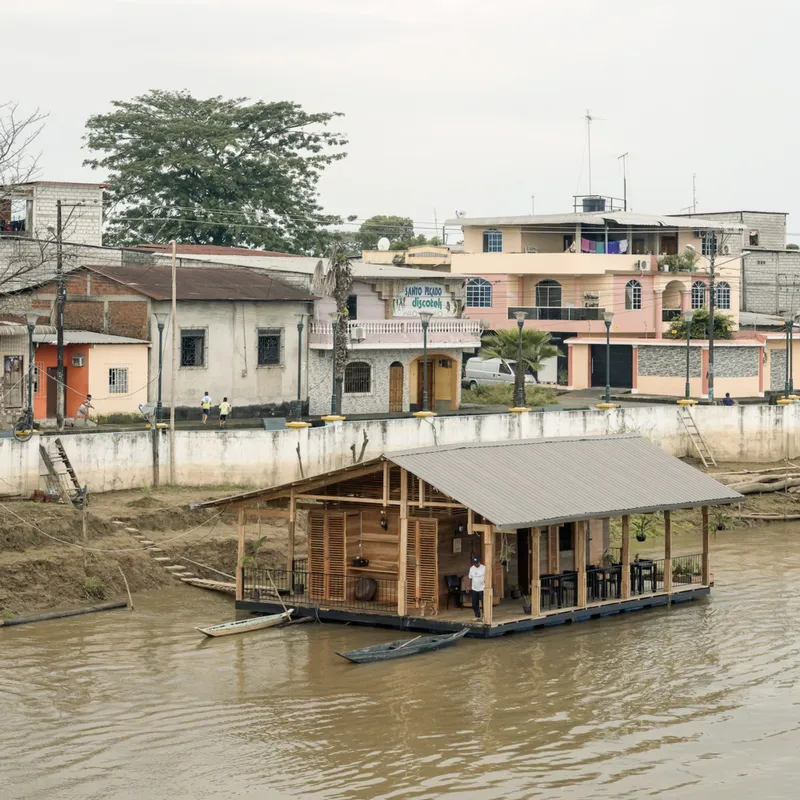 Floating structure with exposed timber frame and slatted wood screens moored near concrete riverbank