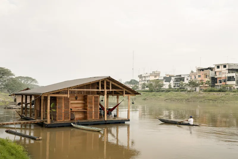 Riverside view of the floating pavilion with gabled roof as a canoe passes in calm water