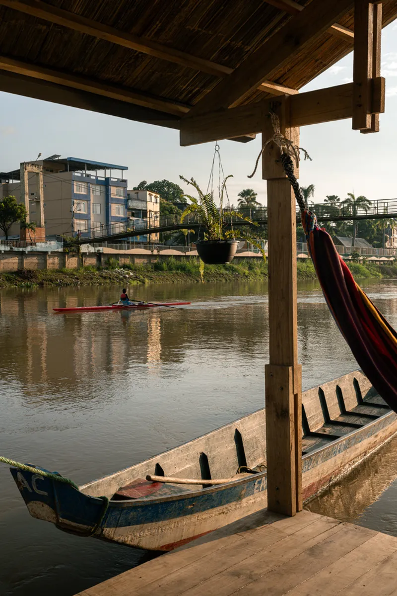 View from beneath the timber roof overhang with hammock and wooden canoe at the water's edge