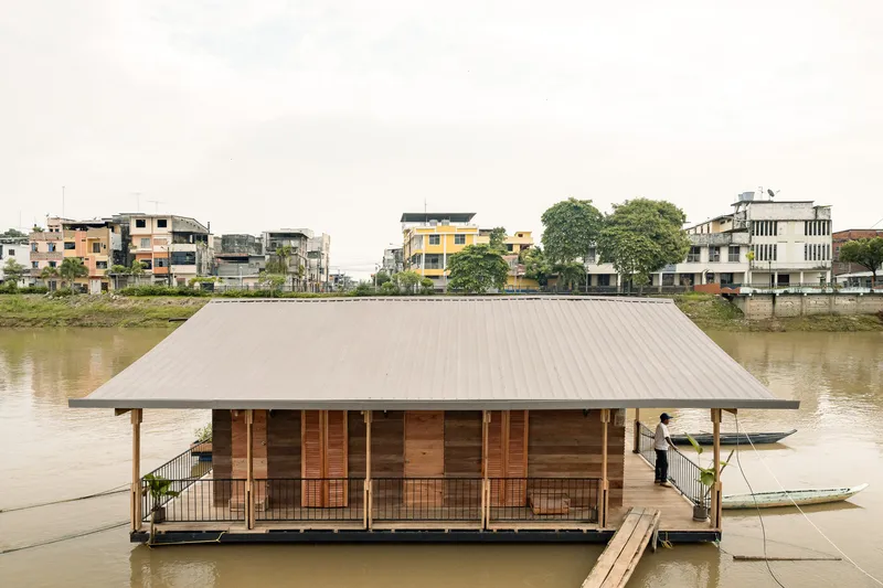 Metal-roofed floating structure with timber walls and perimeter deck moored along a residential waterfront