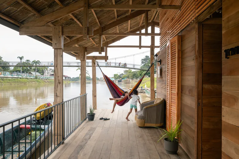 Covered timber deck with exposed roof framing and hammock hung between columns overlooking the river