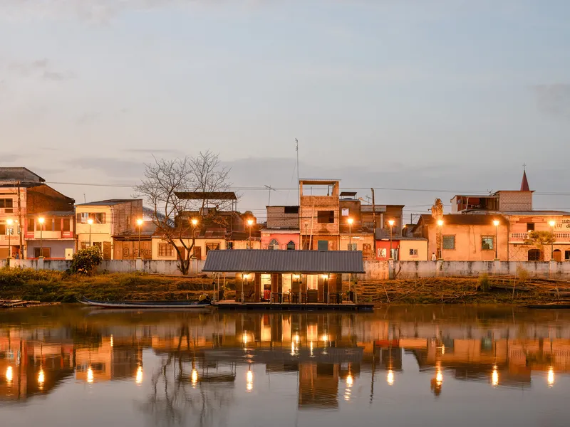 Illuminated floating pavilion reflected in still river water at dusk with streetlights glowing on the far bank