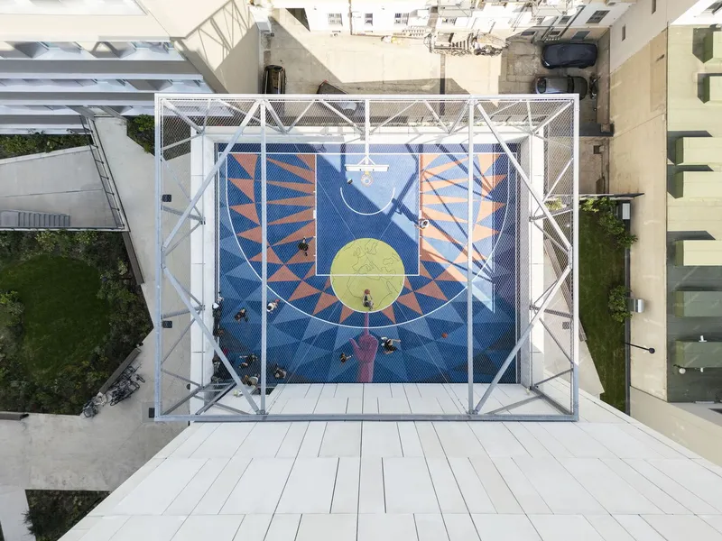 Top-down view of the rooftop basketball court enclosed by white steel structural frame with people playing