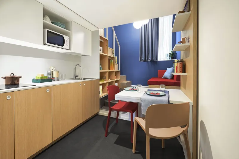 Combined kitchenette and study area with blue painted alcove and red dining chairs beneath daylight
