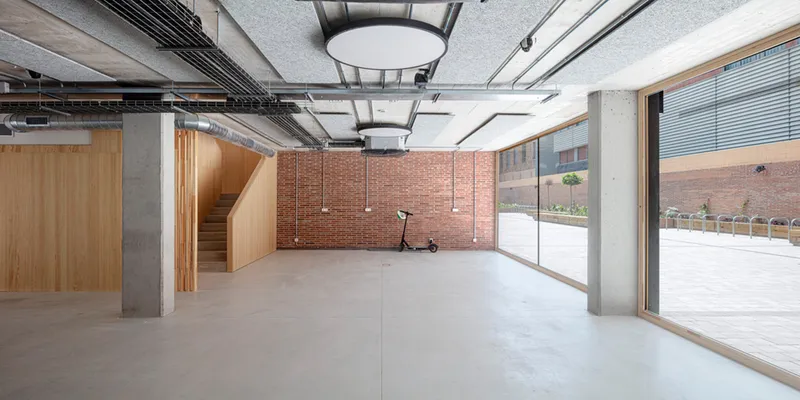 Interior space with exposed concrete columns, red brick wall and large glazed doors to courtyard