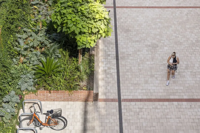 Overhead view of paver plaza with planted bed, parked bicycle and a person walking in shadow