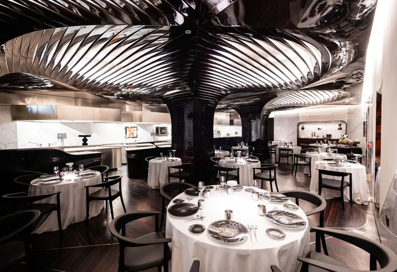 Dining room with ribbed metallic ceiling panels arching over round tables set with white linens