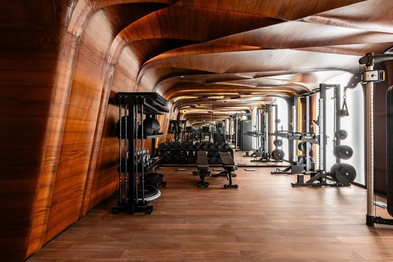 Fitness room with undulating wood-clad ceiling and walls over exercise equipment and timber flooring