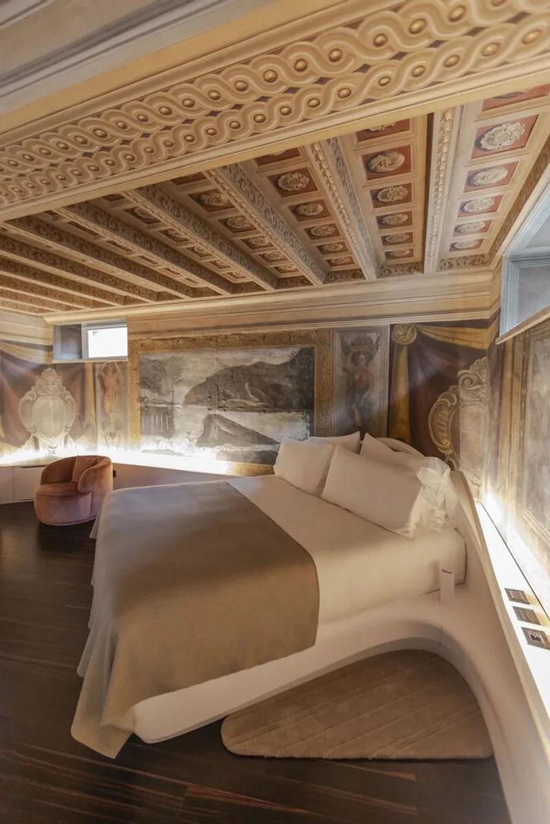 Bedroom with ornate coffered ceiling above a sculpted bed platform and historic wall frescoes