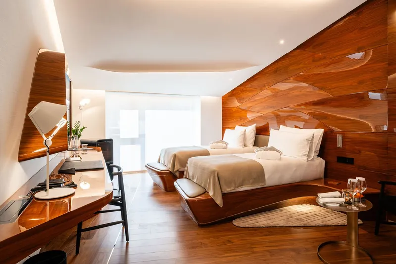Guest room with twin beds against a flowing wood-grain wall panel under cove lighting