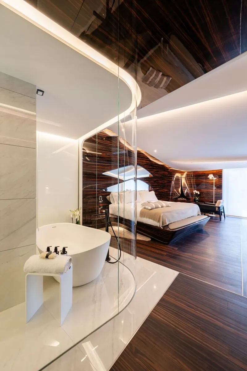 Curved glass partition separating the freestanding bathtub from the striped wood sleeping area