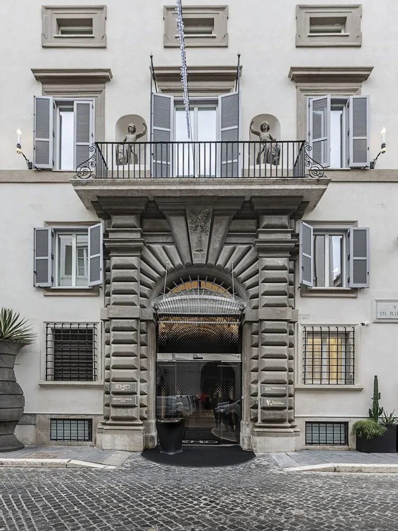 Street facade with rusticated stone entry portal and symmetrical shuttered windows on cobblestone pavement