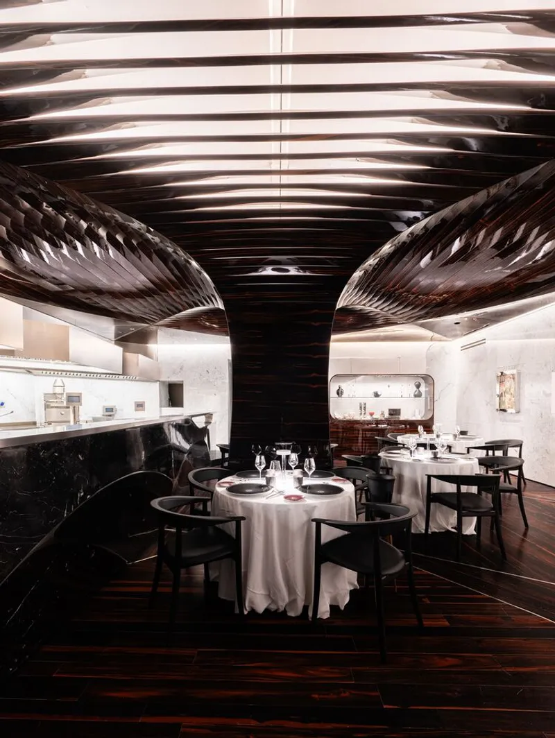 Dining space beneath ribbed metallic ceiling structure with central column wrapped in dark material