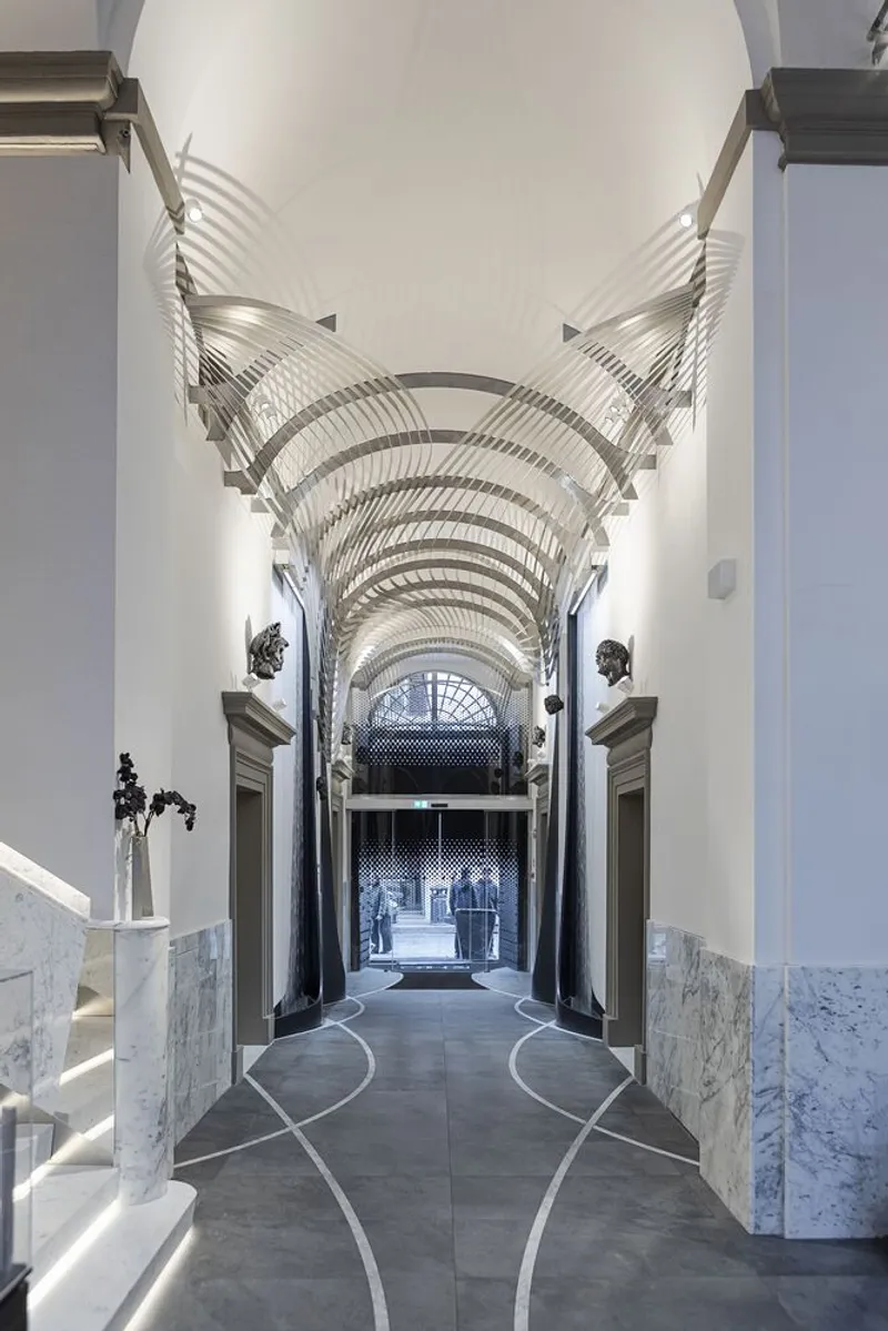 Vaulted corridor with layered metal ceiling ribs and grey stone flooring leading to exterior