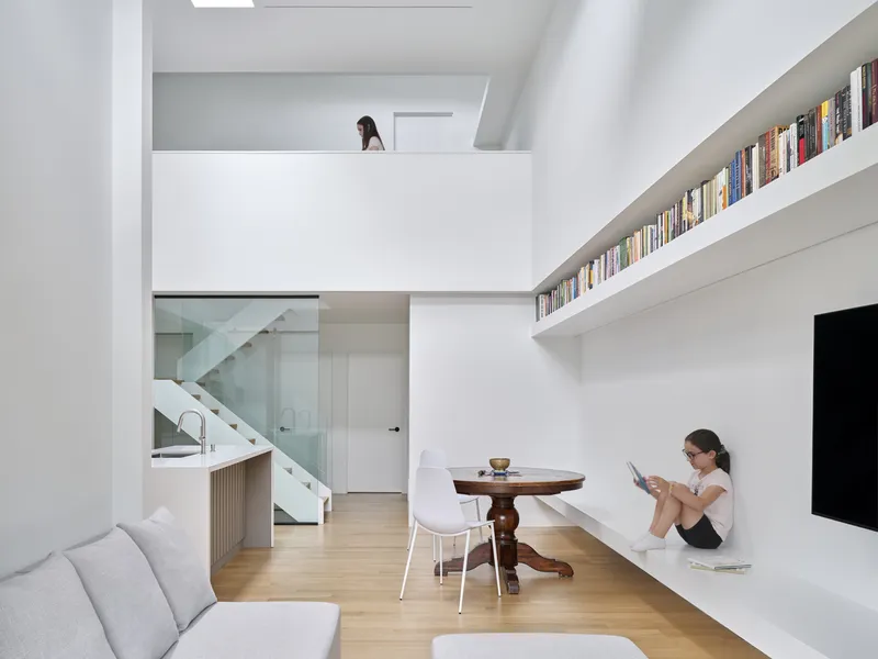 Double-height living space with mezzanine above and person sitting beneath continuous book shelf