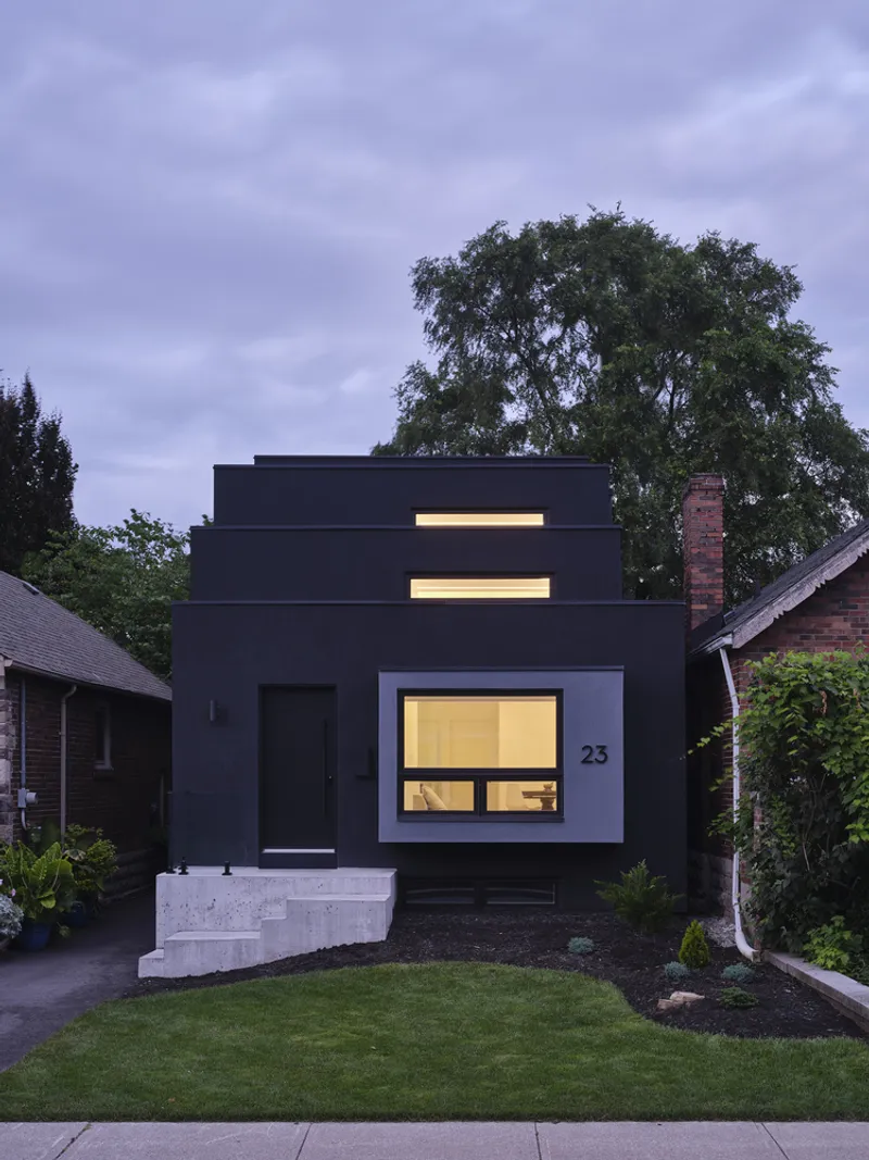 Black facade with illuminated clerestory windows and concrete stoop at dusk